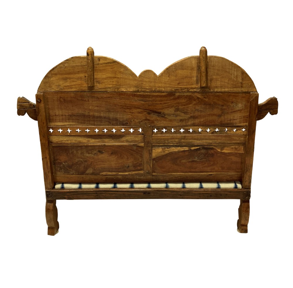 A low carved teak floor seat with arched backrest panels featuring carved bird motifs and a blue and white ikat patterned cushion. View II