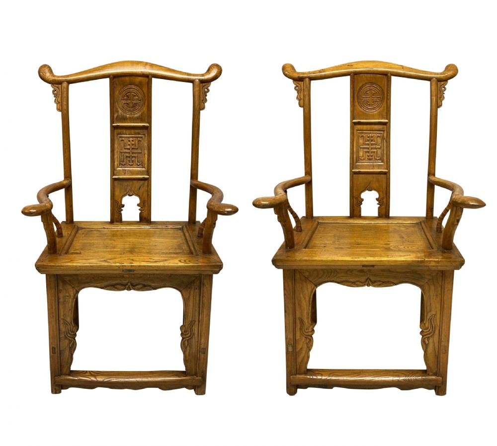 A pair of nineteenth-century Chinese elm yoke-back armchairs featuring carved central back splats and curved armrests.
