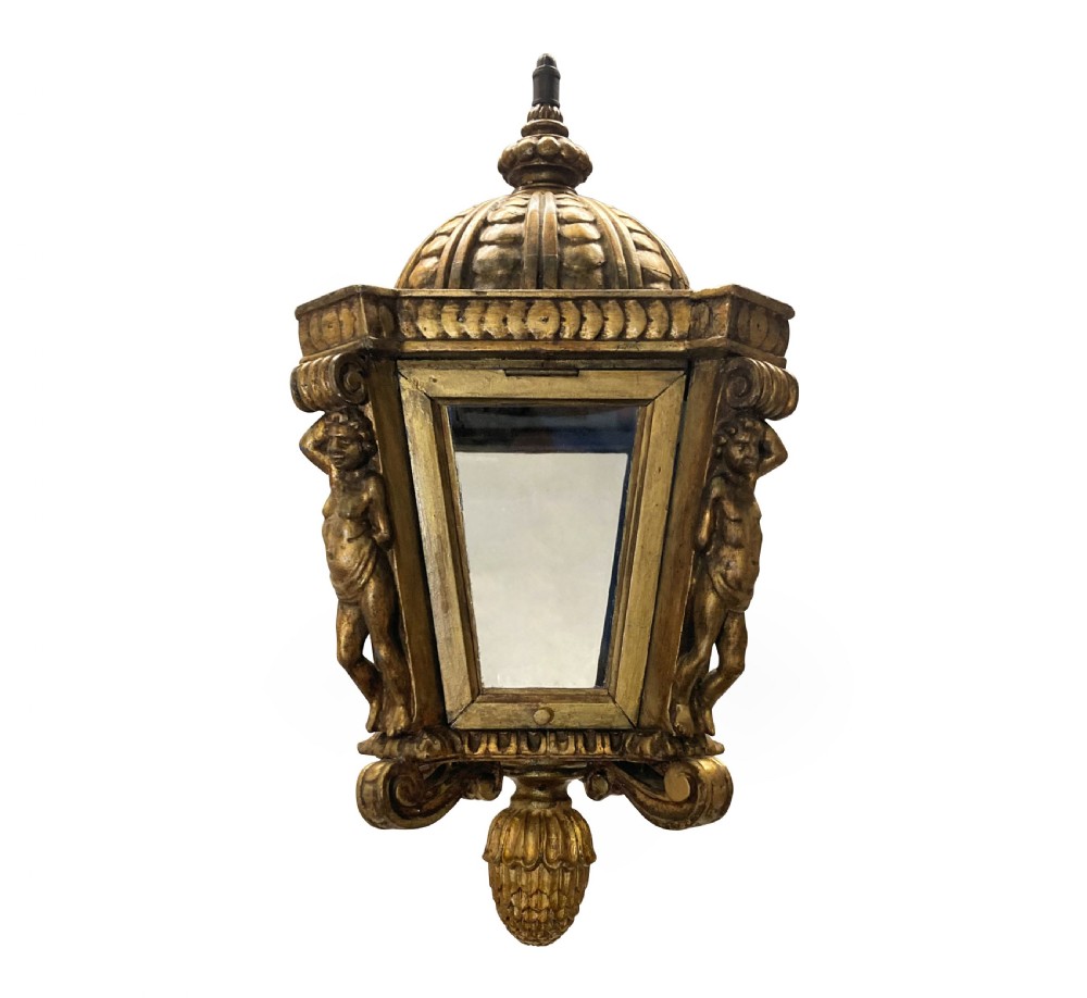 A carved Florentine giltwood hanging lantern with glazed glass panels, flanked by sculpted figures and capped with a domed top and pinecone drop.