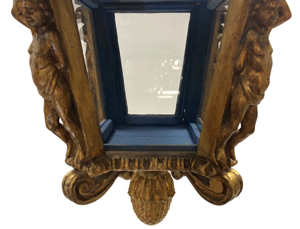A carved Florentine giltwood hanging lantern with glazed glass panels, flanked by sculpted figures and capped with a domed top and pinecone drop. View V