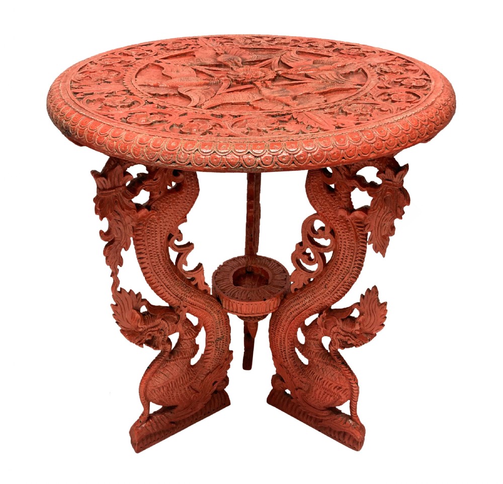 A circular red Chinese side table featuring carved cinnabar lacquered relief patterns on the top and three legs shaped as dragons.