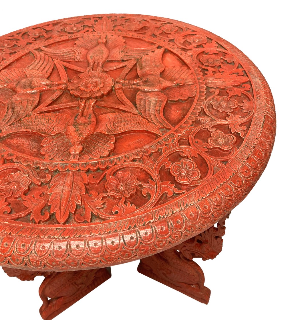 A circular red Chinese side table featuring carved cinnabar lacquered relief patterns on the top and three legs shaped as dragons. View V