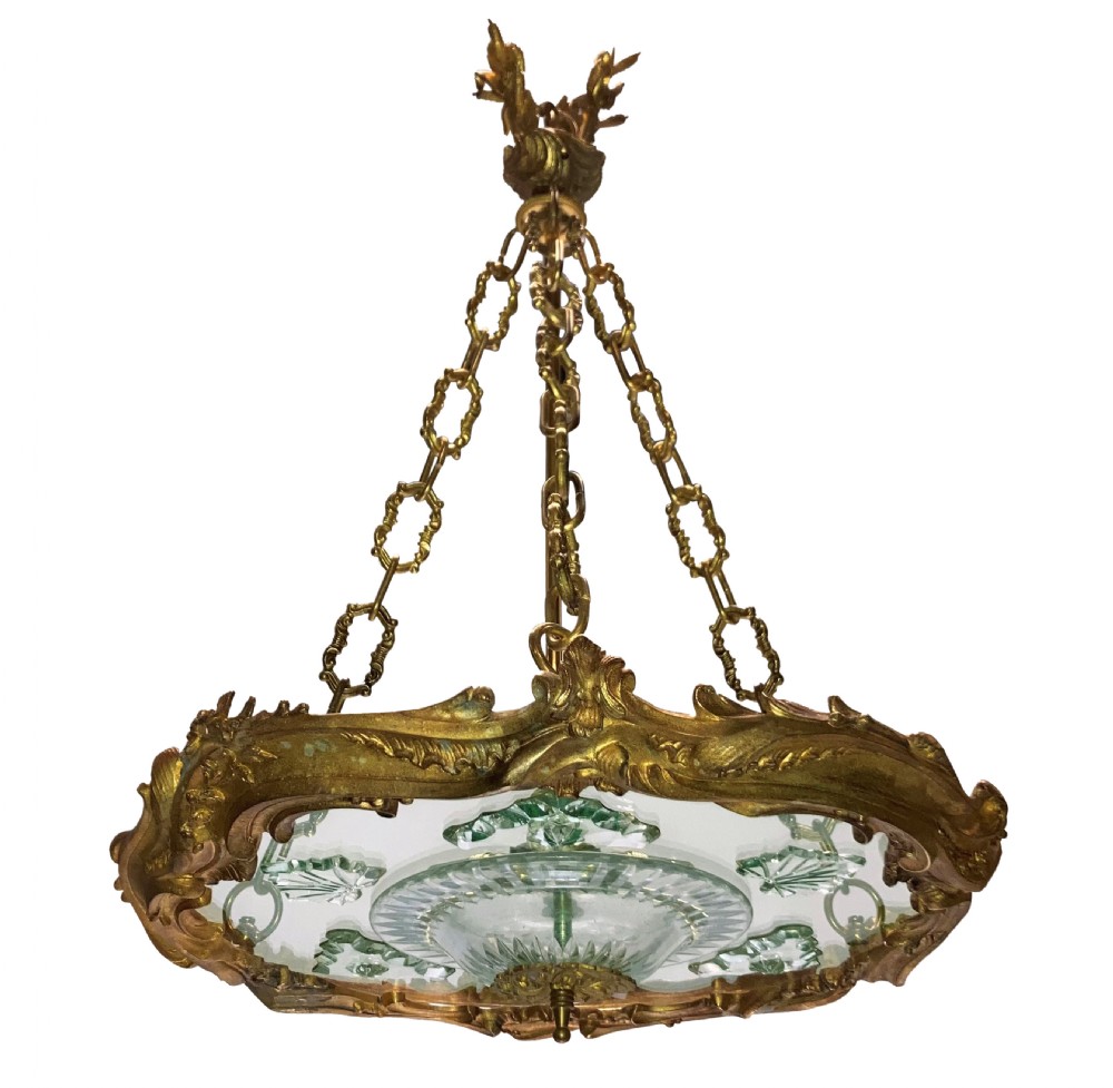 A French Rococo style light fixture featuring a gold-toned ormolu frame with scrolling foliate designs surrounding a central cut-glass bowl suspended by three decorative metal chains.