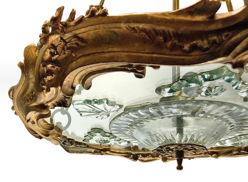 A French Rococo style light fixture featuring a gold-toned ormolu frame with scrolling foliate designs surrounding a central cut-glass bowl suspended by three decorative metal chains. View IV
