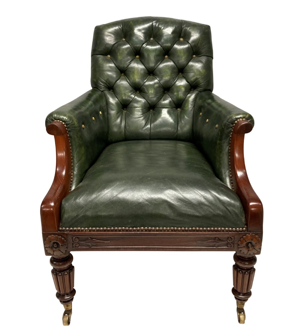 An antique William IV library chair upholstered in deep-buttoned green leather with brass stud trim and carved mahogany legs on brass castors.