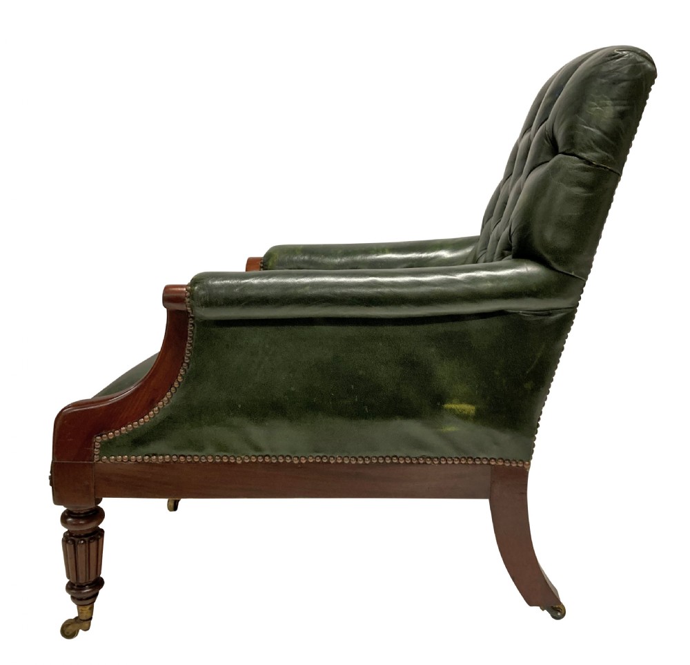An antique William IV library chair upholstered in deep-buttoned green leather with brass stud trim and carved mahogany legs on brass castors. View III
