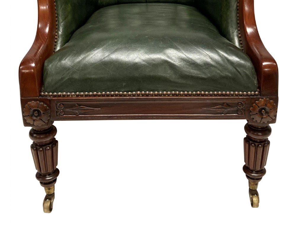 An antique William IV library chair upholstered in deep-buttoned green leather with brass stud trim and carved mahogany legs on brass castors. View IV