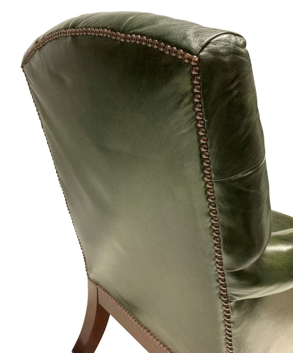 An antique William IV library chair upholstered in deep-buttoned green leather with brass stud trim and carved mahogany legs on brass castors. View V