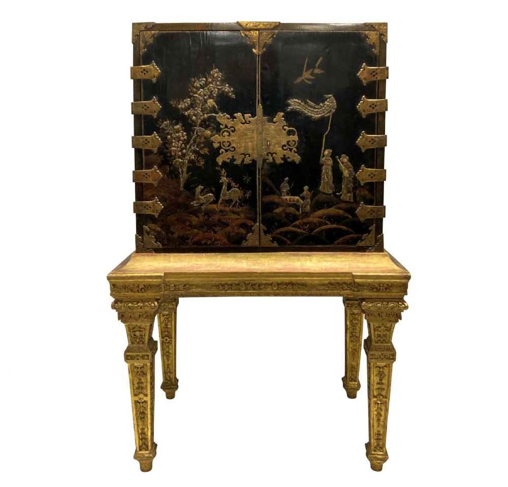 A two-door black japanned cabinet decorated with gold Chinoiserie scenes resting on a carved gilded wooden stand.