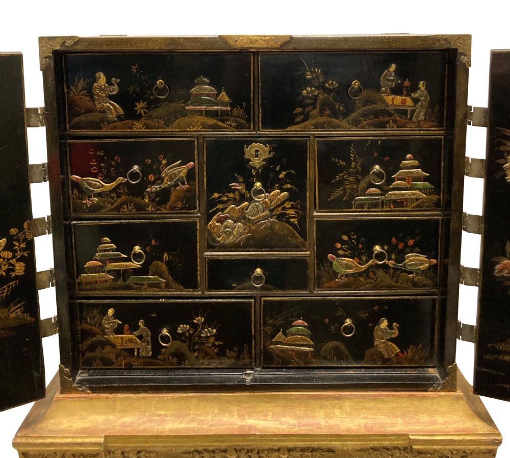 A two-door black japanned cabinet decorated with gold Chinoiserie scenes resting on a carved gilded wooden stand. View V