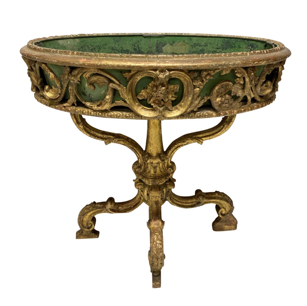 An early 19th-century carved giltwood circular jardiniere featuring scrollwork moulding, a green painted metal liner, and a sculpted tripod base.