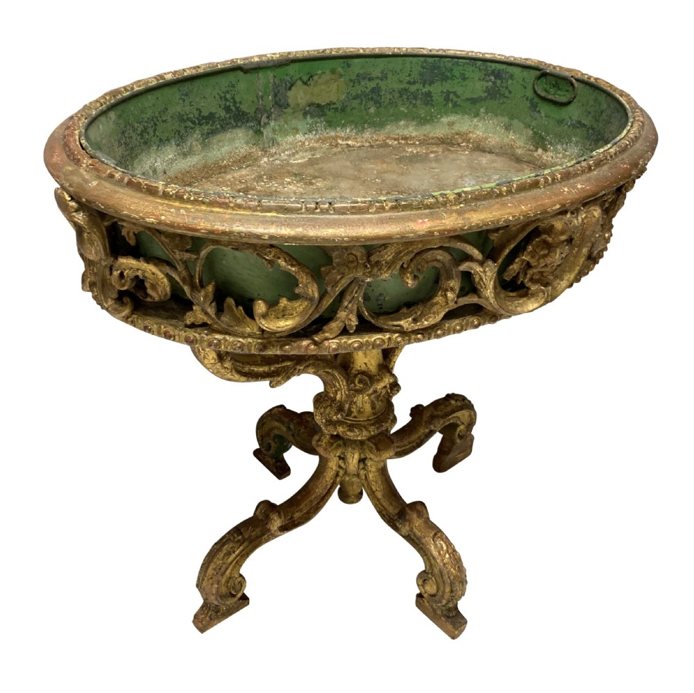 An early 19th-century carved giltwood circular jardiniere featuring scrollwork moulding, a green painted metal liner, and a sculpted tripod base. View V