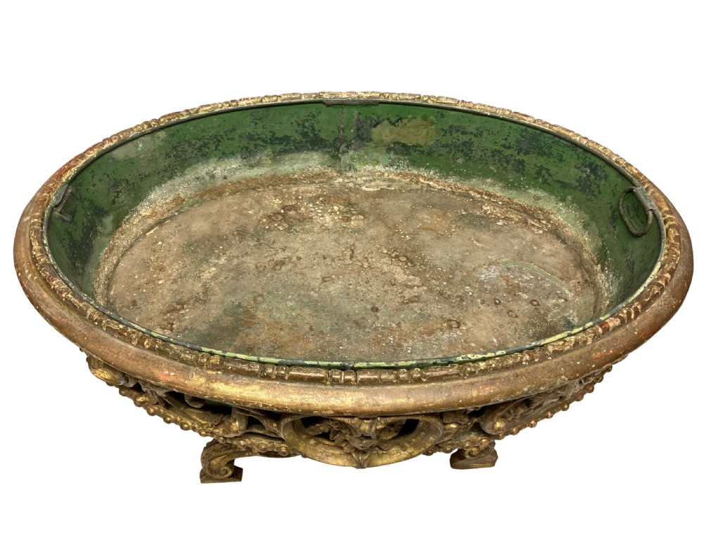 An early 19th-century carved giltwood circular jardiniere featuring scrollwork moulding, a green painted metal liner, and a sculpted tripod base. View VI