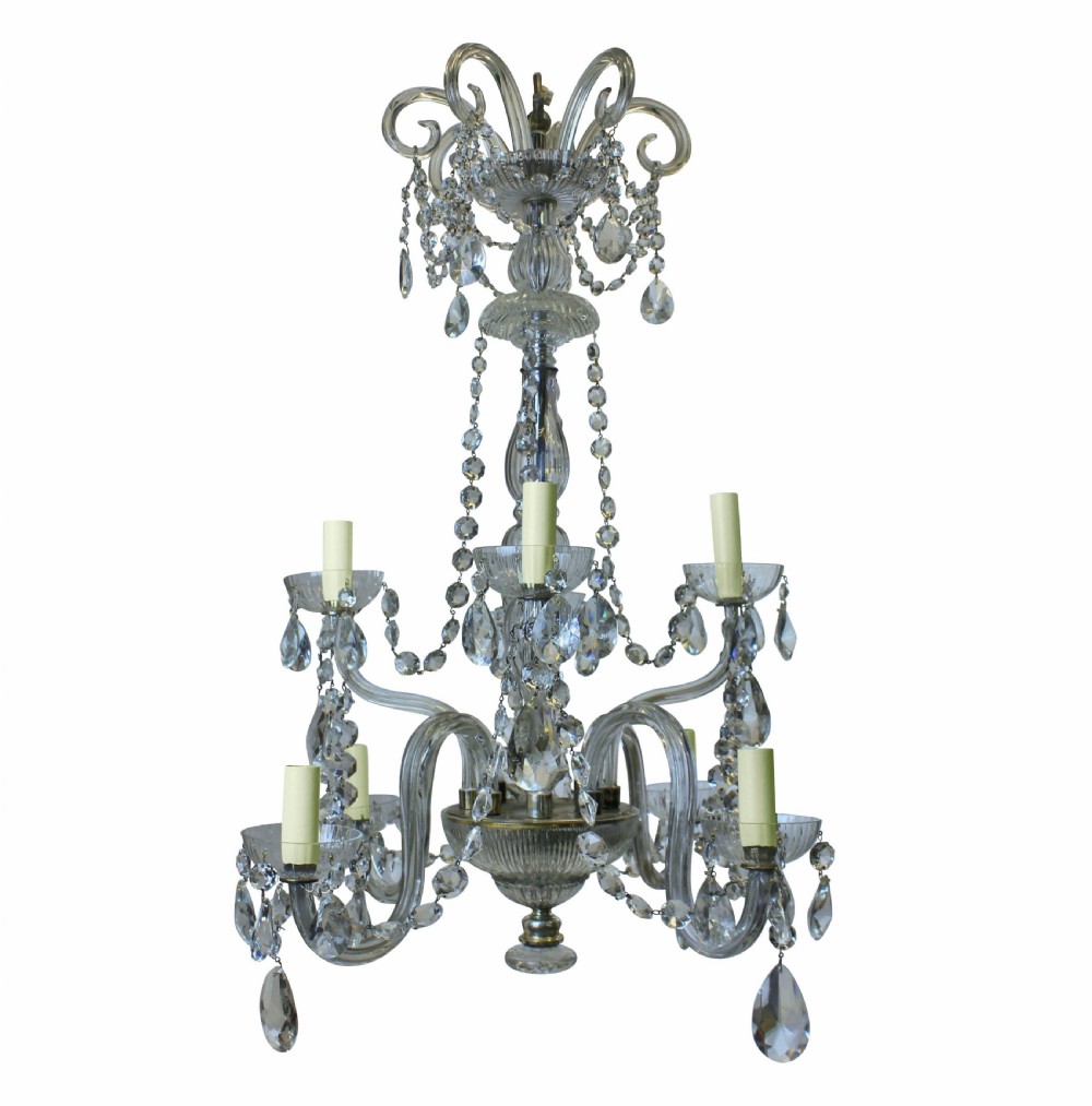 An Edwardian cut glass chandelier featuring eight scrolling arms, candle-style lamp holders, suspended teardrop crystals, and a tiered central column.