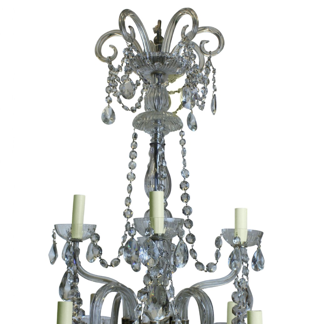 An Edwardian cut glass chandelier featuring eight scrolling arms, candle-style lamp holders, suspended teardrop crystals, and a tiered central column. View II