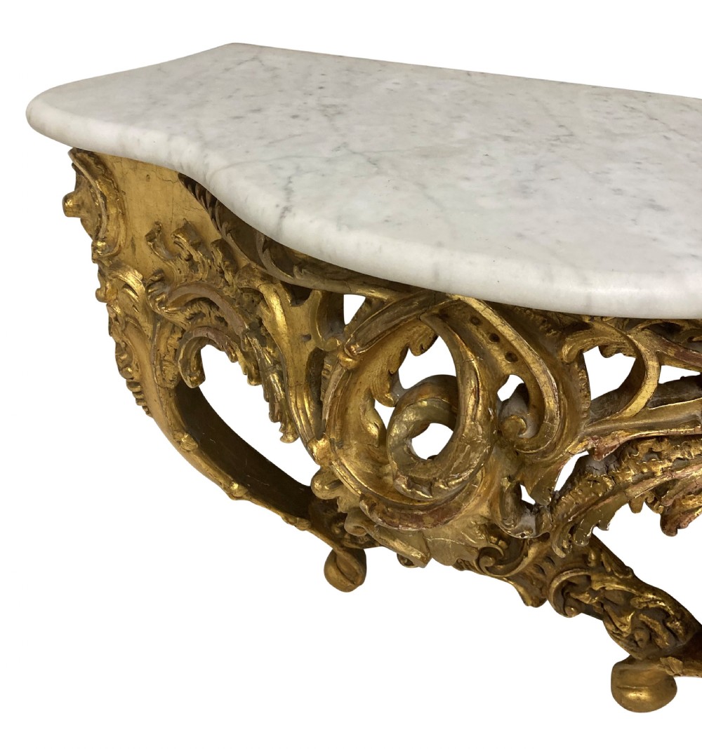 A 19th-century German Rococo Revival carved giltwood console table featuring an openwork scrolled apron and a serpentine white marble top. View V