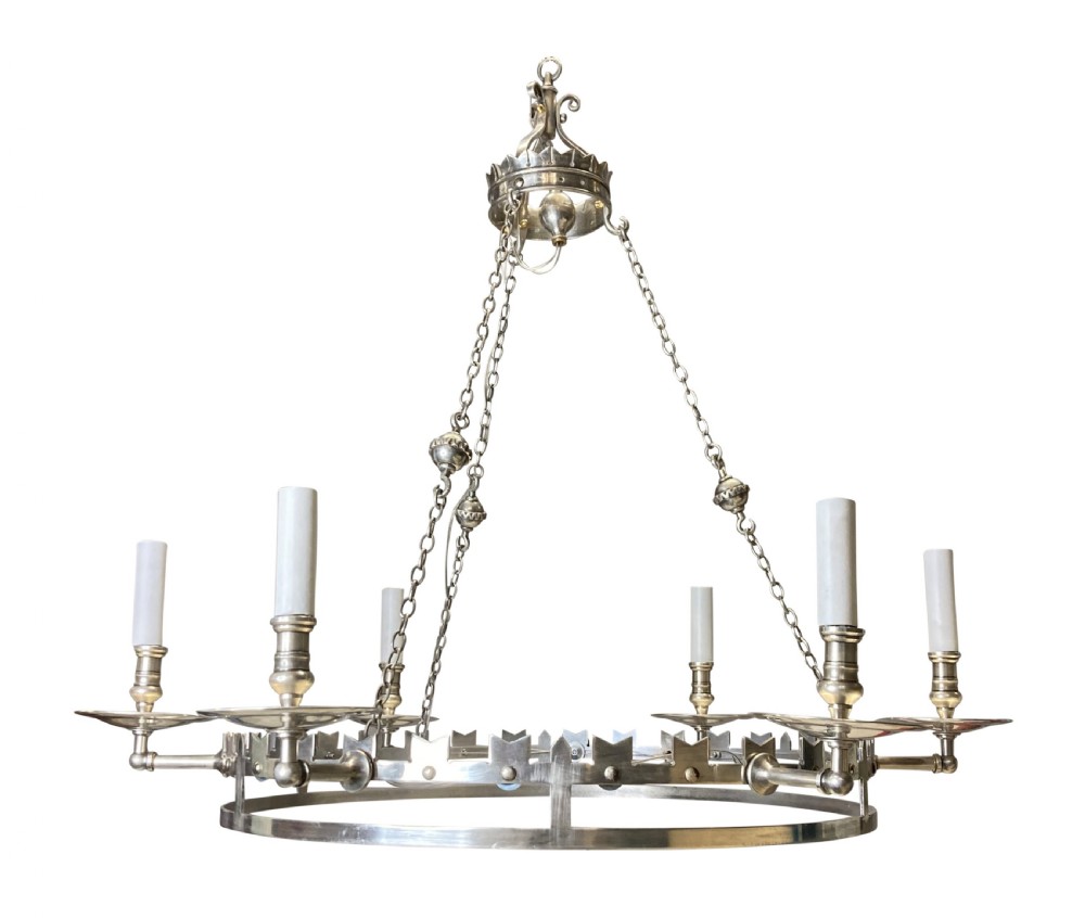 A circular silver-plated Gothic corona light fixture featuring a castellated upper rim, multiple candle-style light holders, and suspension chains leading to a crown-shaped ceiling rose.