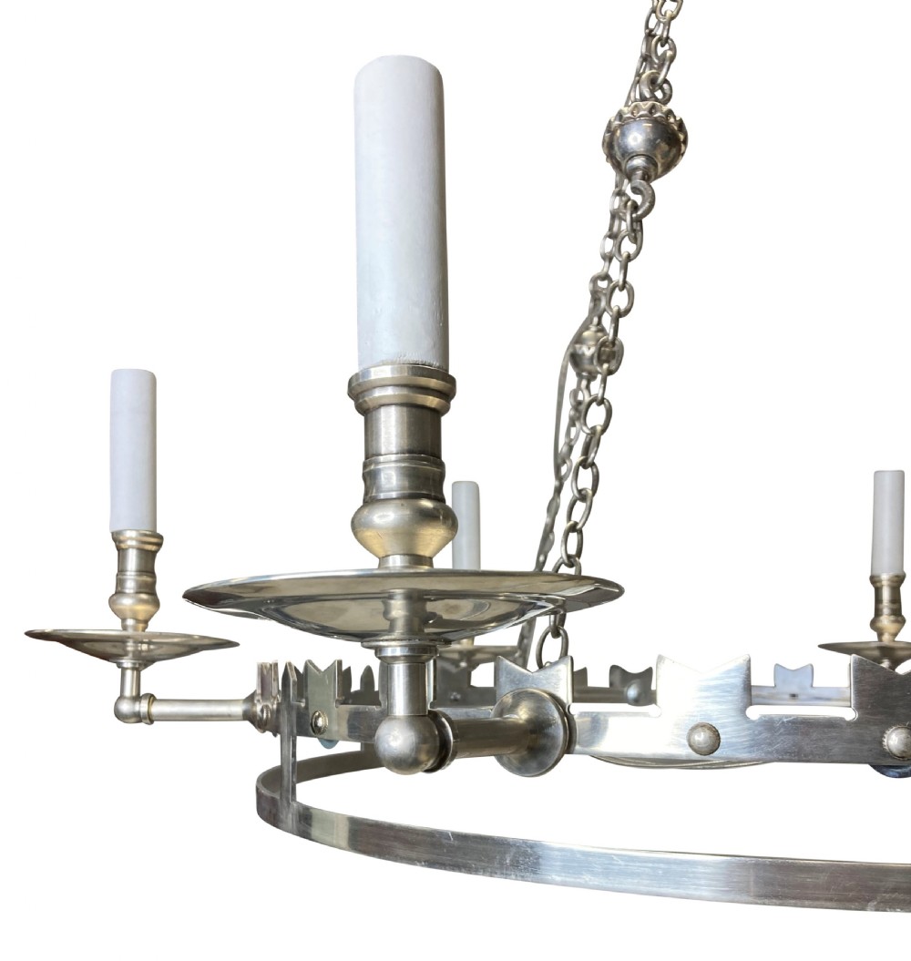 A circular silver-plated Gothic corona light fixture featuring a castellated upper rim, multiple candle-style light holders, and suspension chains leading to a crown-shaped ceiling rose. View III