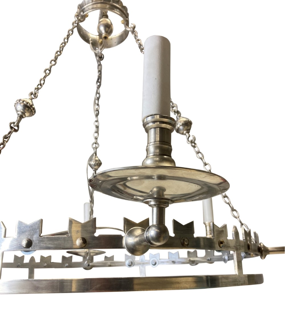 A circular silver-plated Gothic corona light fixture featuring a castellated upper rim, multiple candle-style light holders, and suspension chains leading to a crown-shaped ceiling rose. View IV