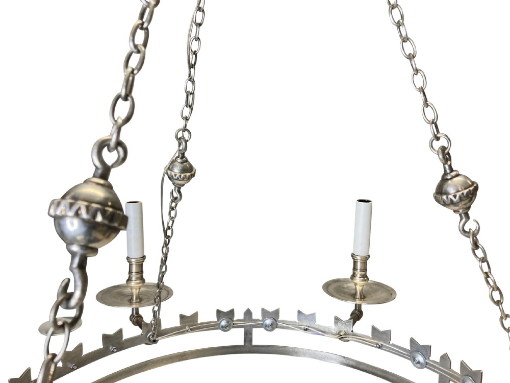 A circular silver-plated Gothic corona light fixture featuring a castellated upper rim, multiple candle-style light holders, and suspension chains leading to a crown-shaped ceiling rose. View VI