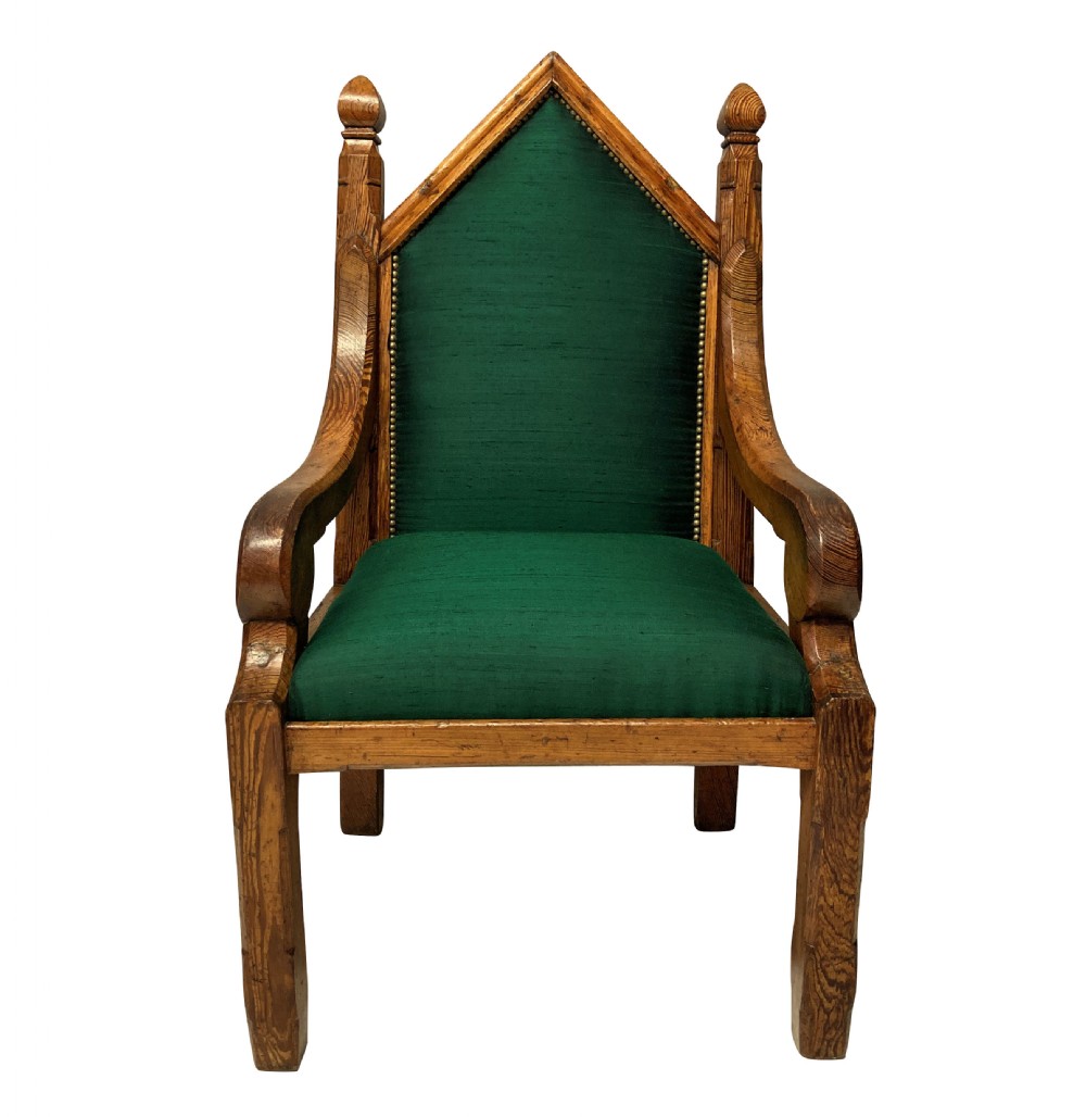 An English Gothic Revival oak armchair featuring a pointed arched backrest upholstered in green fabric with brass stud trimming.