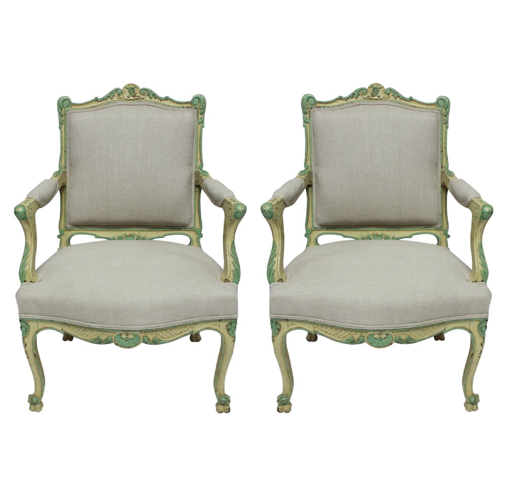 A pair of 1930s Louis XV style open armchairs with distressed cream and green painted wooden frames and neutral linen upholstery.
