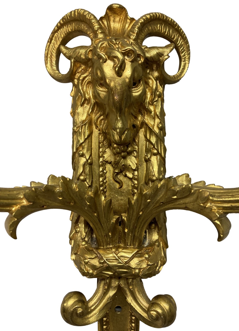 A pair of gilt brass Regency style twin-arm wall sconces featuring ram head central backplates and white candle sleeves. View VII