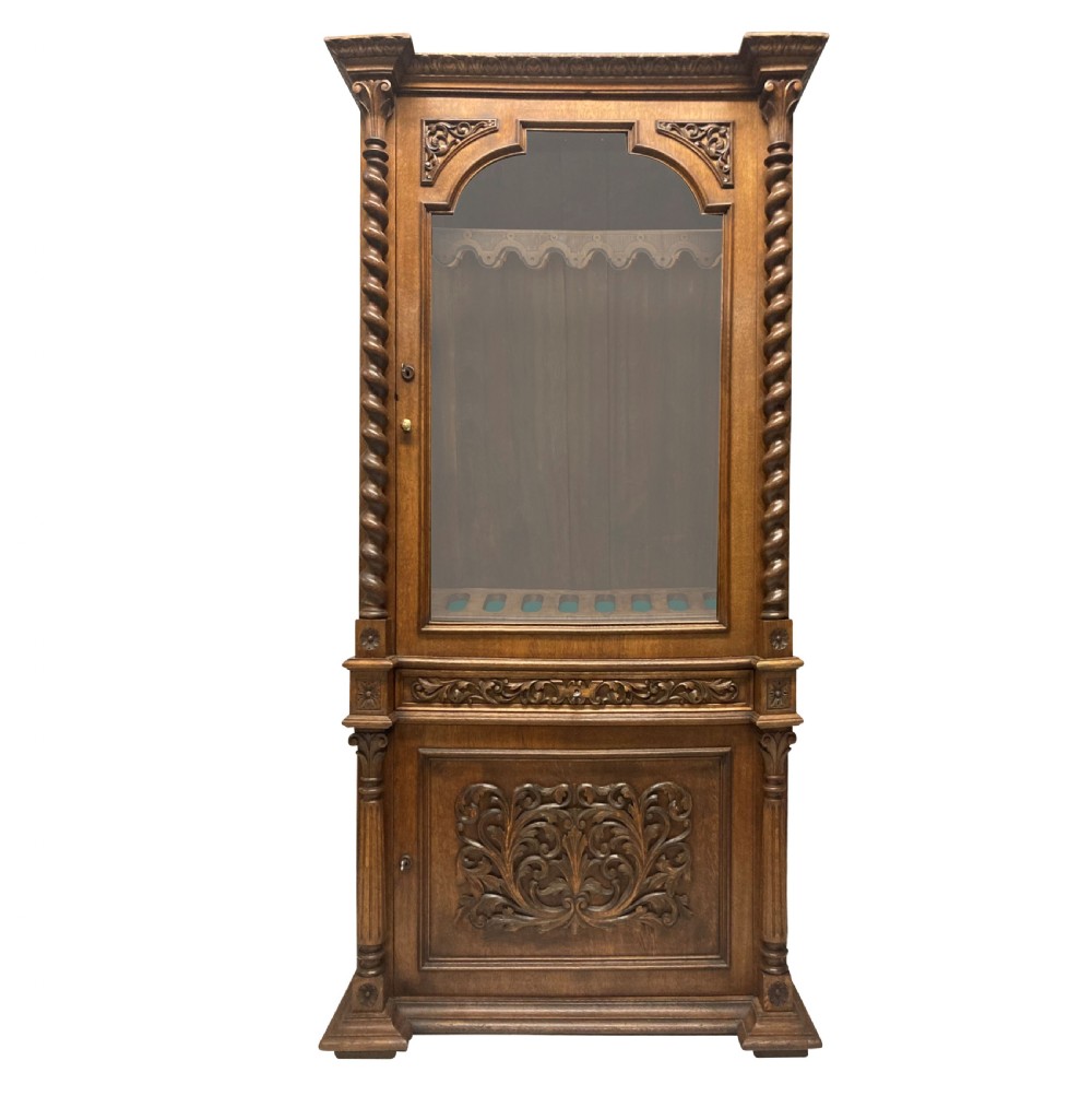 A nineteenth-century carved oak gun cabinet featuring spiralled barley twist columns, a glazed upper door, and relief-carved botanical motifs on the lower door.