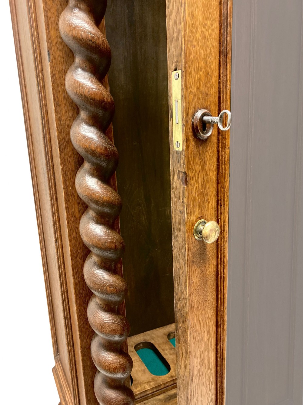 A nineteenth-century carved oak gun cabinet featuring spiralled barley twist columns, a glazed upper door, and relief-carved botanical motifs on the lower door. View II