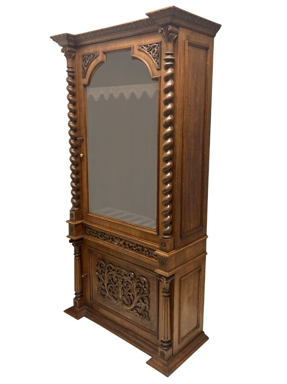 A nineteenth-century carved oak gun cabinet featuring spiralled barley twist columns, a glazed upper door, and relief-carved botanical motifs on the lower door. View VI