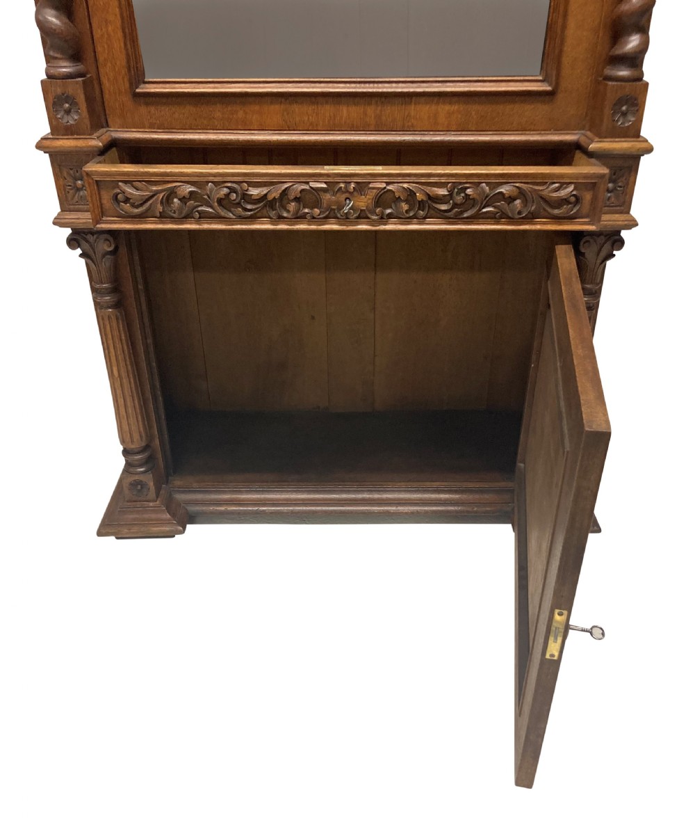 A nineteenth-century carved oak gun cabinet featuring spiralled barley twist columns, a glazed upper door, and relief-carved botanical motifs on the lower door. View X