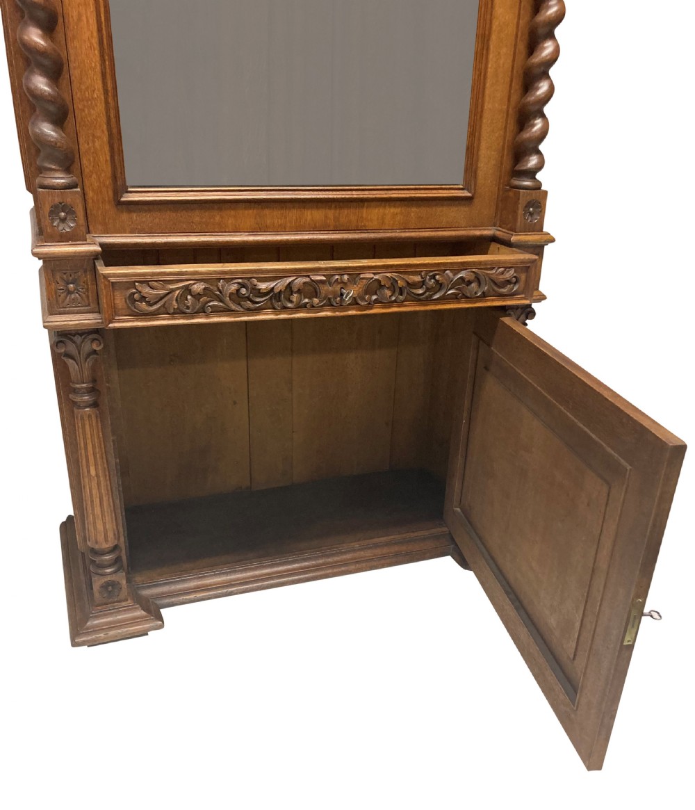 A nineteenth-century carved oak gun cabinet featuring spiralled barley twist columns, a glazed upper door, and relief-carved botanical motifs on the lower door. View XI