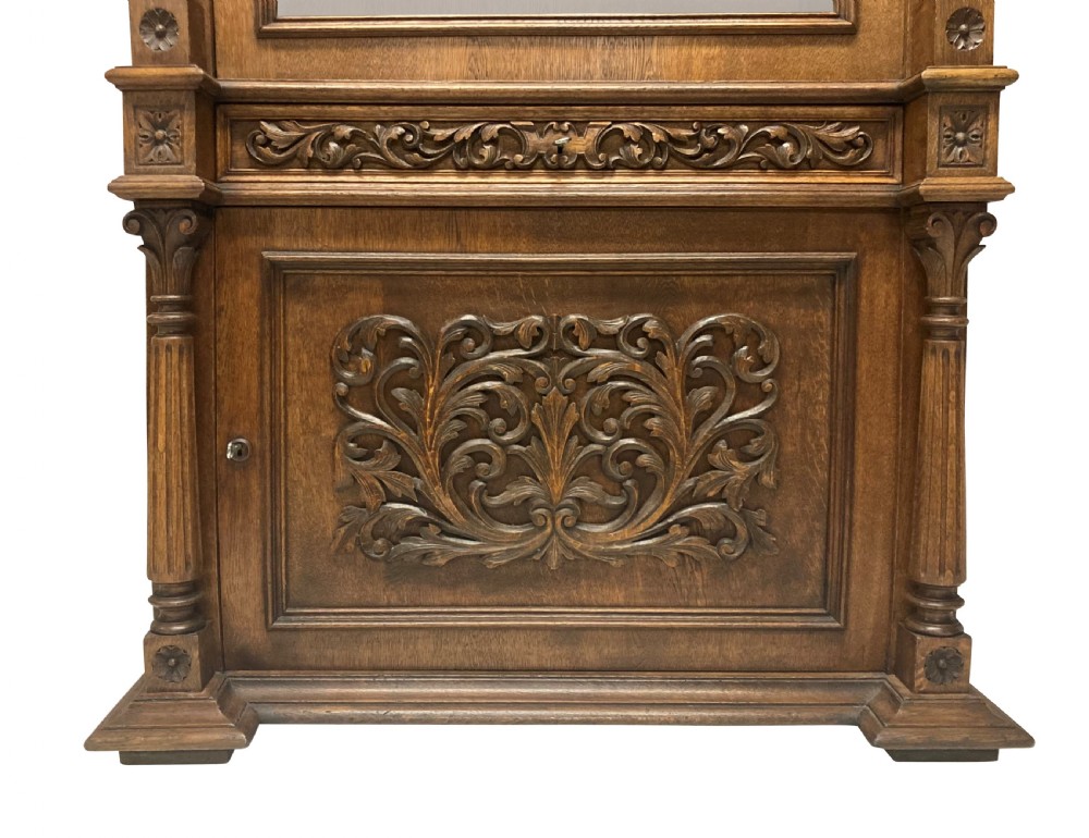 A nineteenth-century carved oak gun cabinet featuring spiralled barley twist columns, a glazed upper door, and relief-carved botanical motifs on the lower door. View XIII