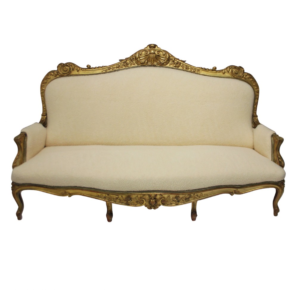 An early nineteenth-century giltwood settee featuring a carved cresting rail, cabriole legs, and cream upholstery.