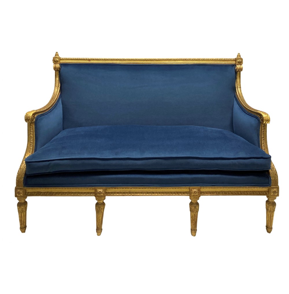 A French Louis XVI style settee featuring a carved giltwood frame with tapered fluted legs and blue velvet cushion upholstery.
