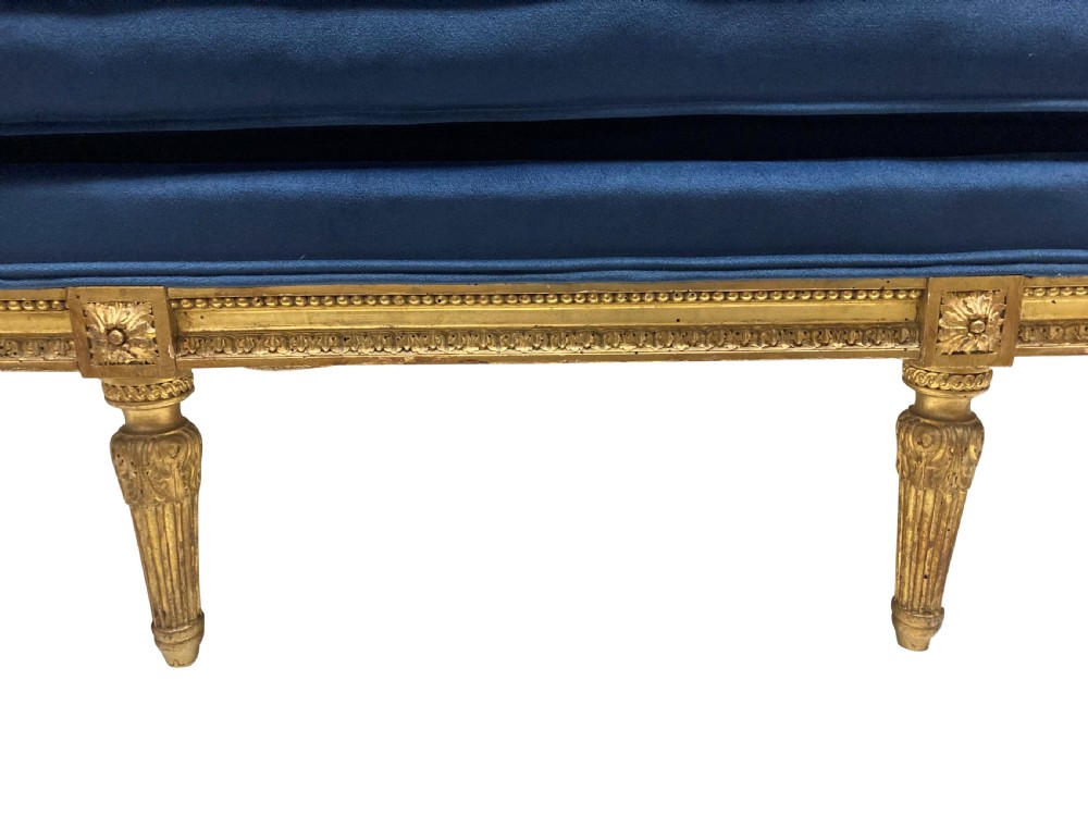 A French Louis XVI style settee featuring a carved giltwood frame with tapered fluted legs and blue velvet cushion upholstery. View VI