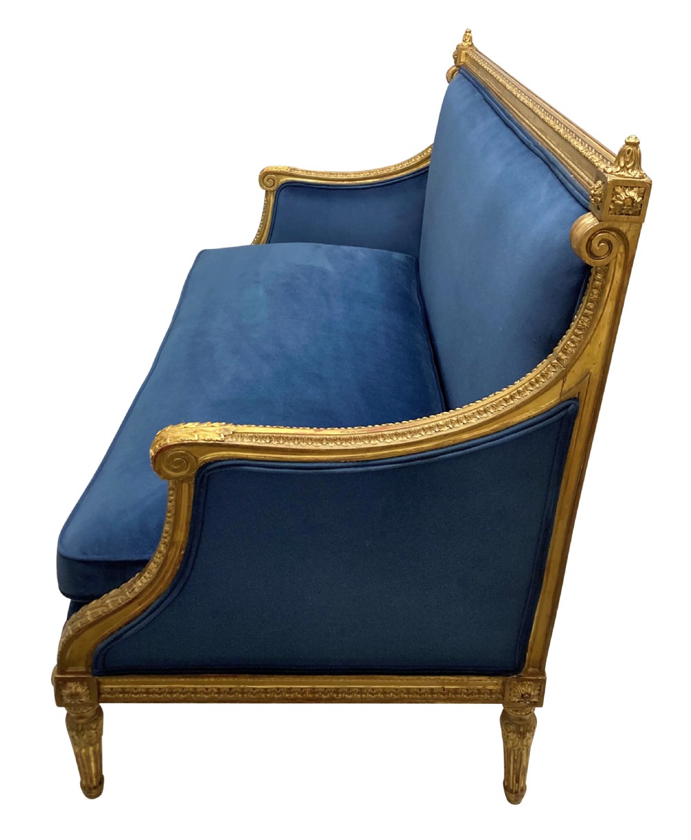 A French Louis XVI style settee featuring a carved giltwood frame with tapered fluted legs and blue velvet cushion upholstery. View VII
