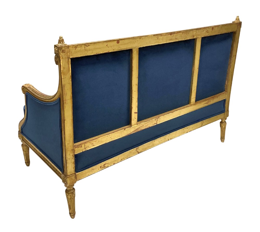 A French Louis XVI style settee featuring a carved giltwood frame with tapered fluted legs and blue velvet cushion upholstery. View VIII
