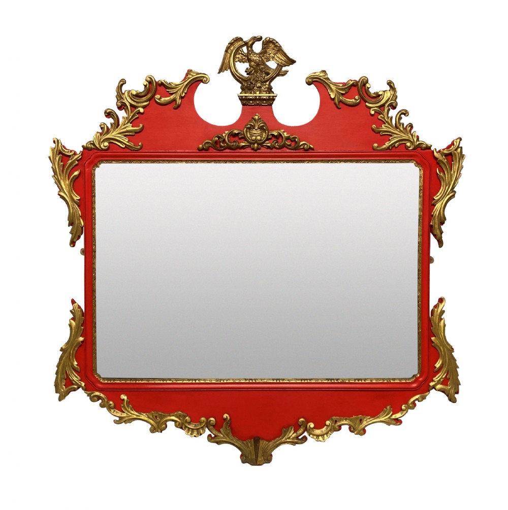 A George II style horizontal wall mirror featuring a scarlet red lacquered frame adorned with intricate giltwood rococo scrollwork and a central eagle crest.