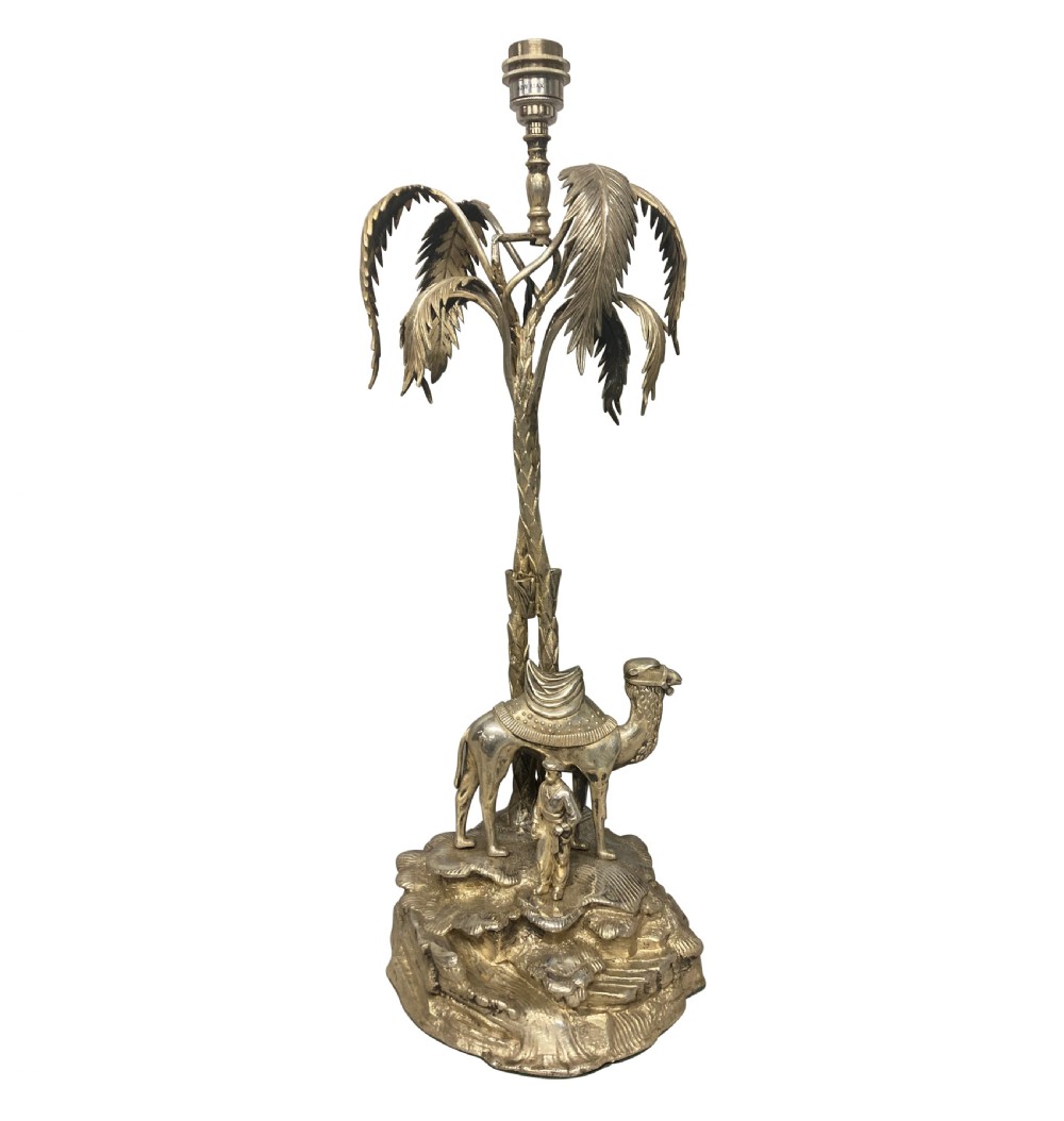 A silver-plated table lamp featuring a sculpted palm tree stem above a camel and figure base.