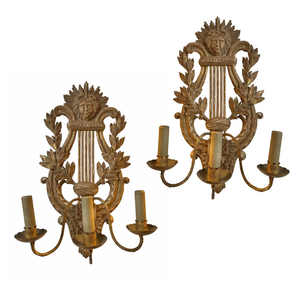 A pair of carved French giltwood wall sconces crafted in the shape of a musical lyre, featuring an Apollo sunburst mask top and three scrolling candle branches.