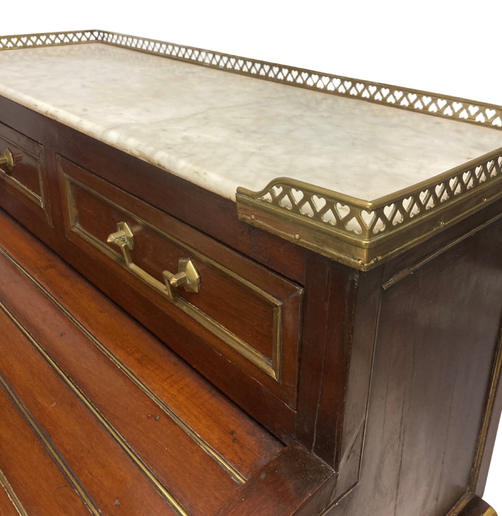 A small Directoire style mahogany cylinder desk with brass inlay trim, a marble top framed by a pierced brass gallery, slatted roll-top cylinder, drawer, and tapered legs. View V