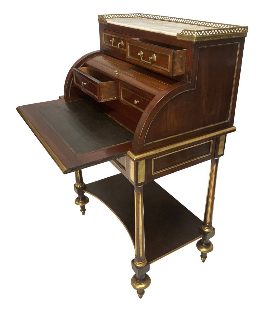 A small Directoire style mahogany cylinder desk with brass inlay trim, a marble top framed by a pierced brass gallery, slatted roll-top cylinder, drawer, and tapered legs. View VII