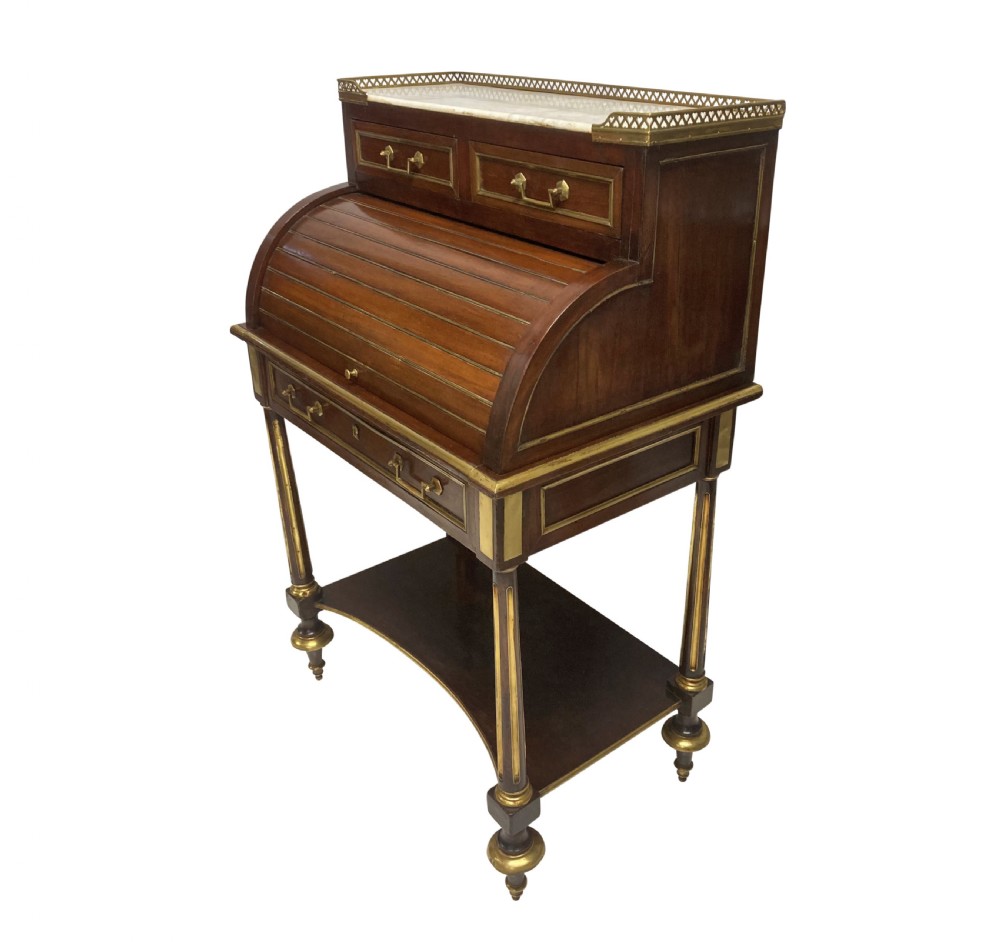 A small Directoire style mahogany cylinder desk with brass inlay trim, a marble top framed by a pierced brass gallery, slatted roll-top cylinder, drawer, and tapered legs. View X