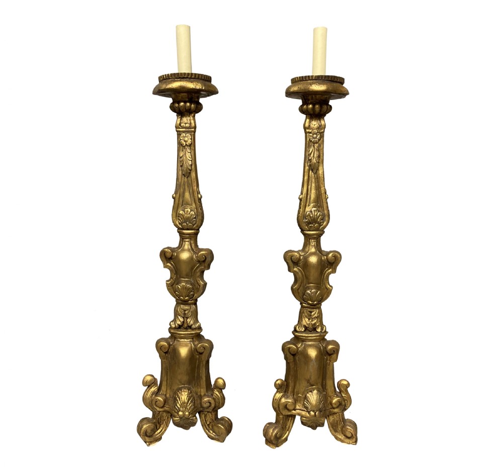 A pair of tall 18th-century Italian carved giltwood table lamps featuring scroll bases, shell carvings, and cream faux candle stems.