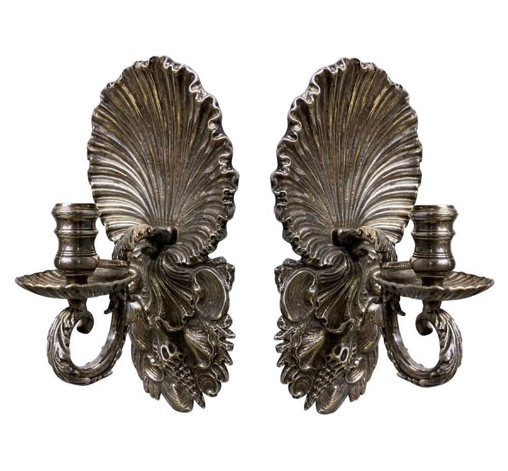 A pair of cast silver grotto style candle sconces featuring detailed scallop shell backplates and scrolling branches.