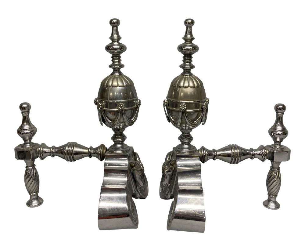 A pair of late 19th-century polished steel fire dogs featuring urn finials with swags, rams head reliefs, and scrolled bases. View III