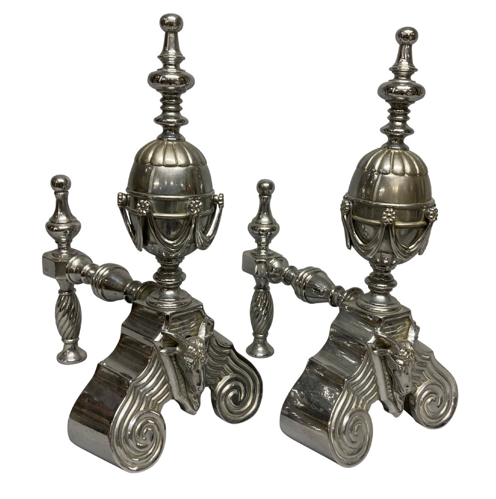 A pair of late 19th-century polished steel fire dogs featuring urn finials with swags, rams head reliefs, and scrolled bases. View IV