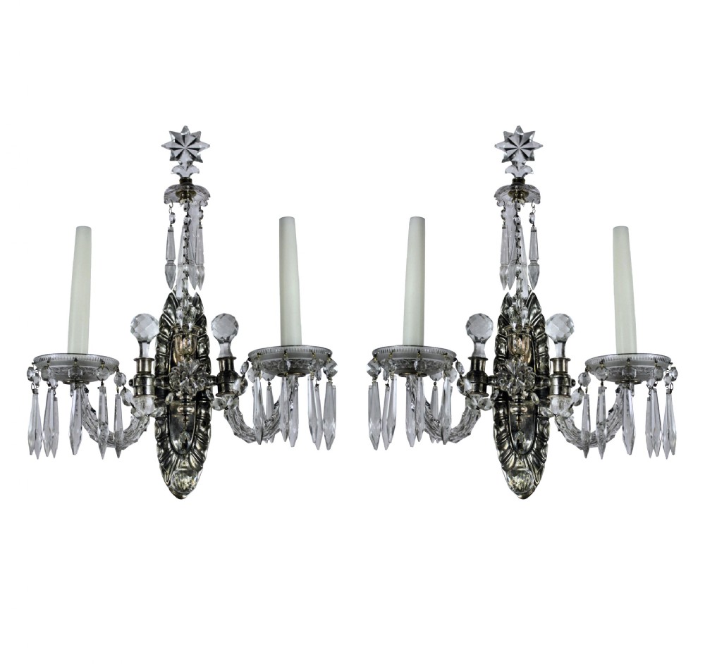 A pair of silver and cut glass twin-branch wall sconces featuring faceted crystal drops, star finials, and candle-style sockets.