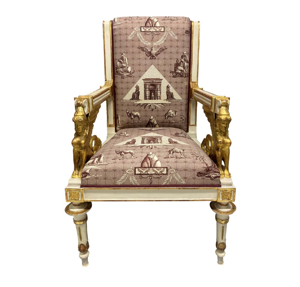 A French Empire armchair featuring a white painted frame with gilt sphinx arm supports and Egyptian revival fabric upholstery.